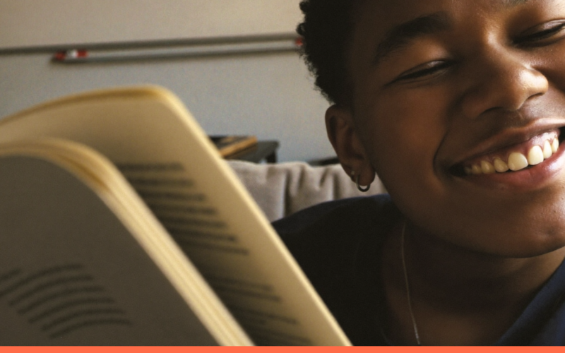 Pessoa relaxada e sorridente aproveitando um dia de folga em casa, no sofá com um livro e uma xícara de chá