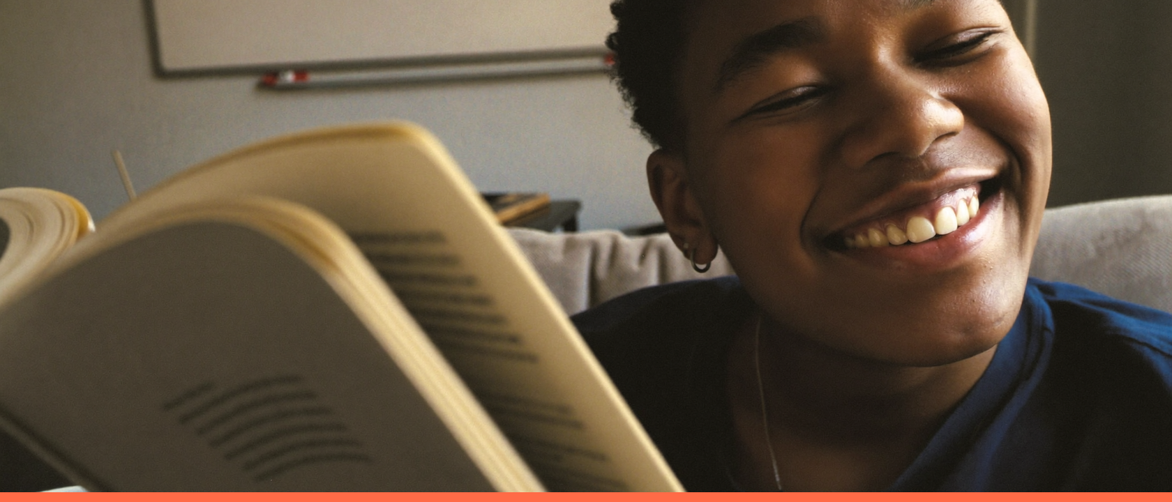 Pessoa relaxada e sorridente aproveitando um dia de folga em casa, no sofá com um livro e uma xícara de chá