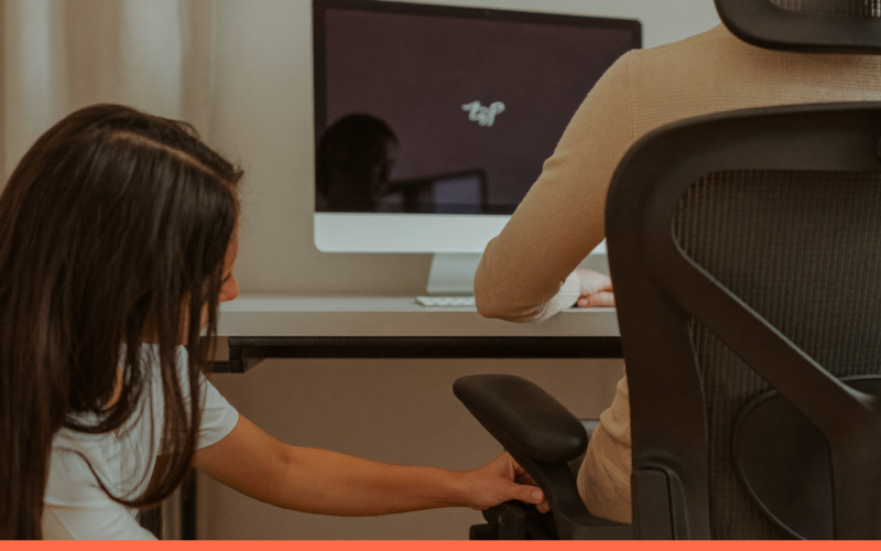 Especialista ajustando a cadeira de uma pessoa no posto de trabalho, com a tela do monitor apagada