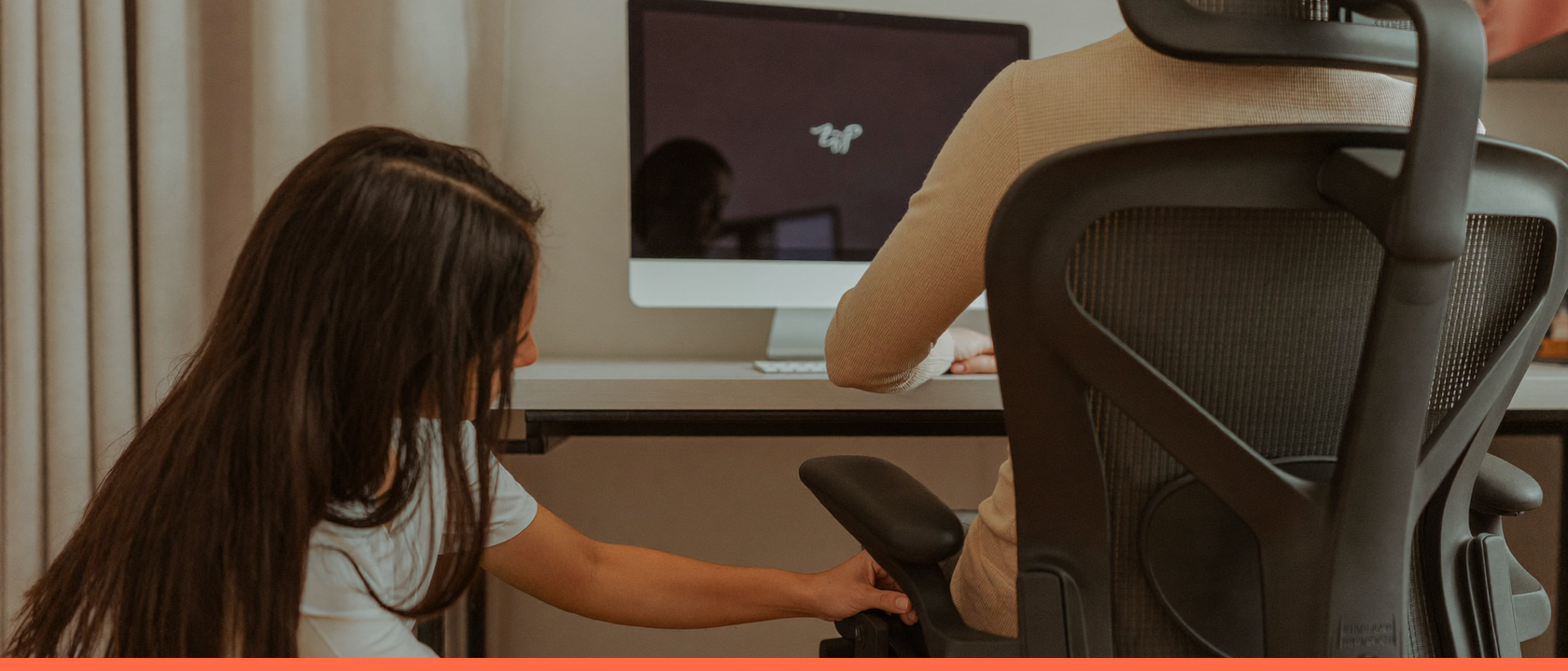 Especialista ajustando a cadeira de uma pessoa no posto de trabalho, com a tela do monitor apagada
