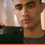 Jovem profissional consultando o celular durante uma pausa curta no corredor do escritório
