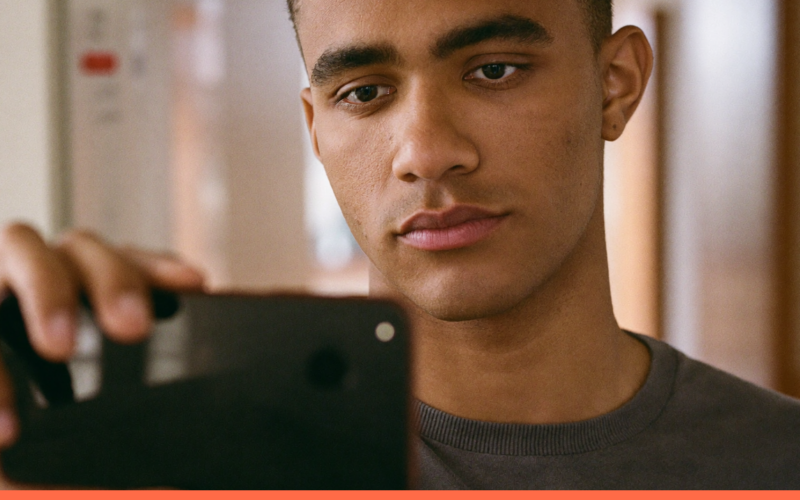 Jovem profissional consultando o celular durante uma pausa curta no corredor do escritório